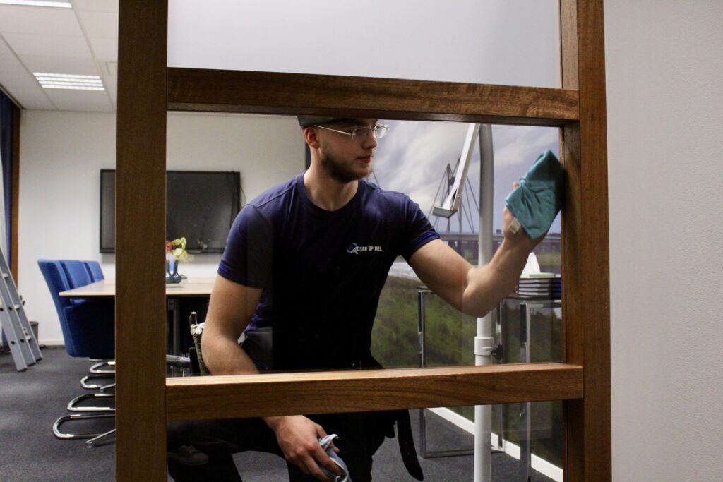 Glazenwasser veegt raam droog met doek in kantoorruimte