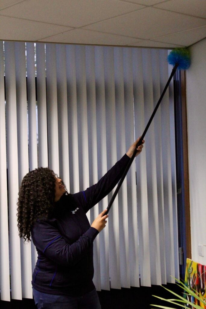 Medewerkster stoft het plafond in kantoorruimte af met een plumeau